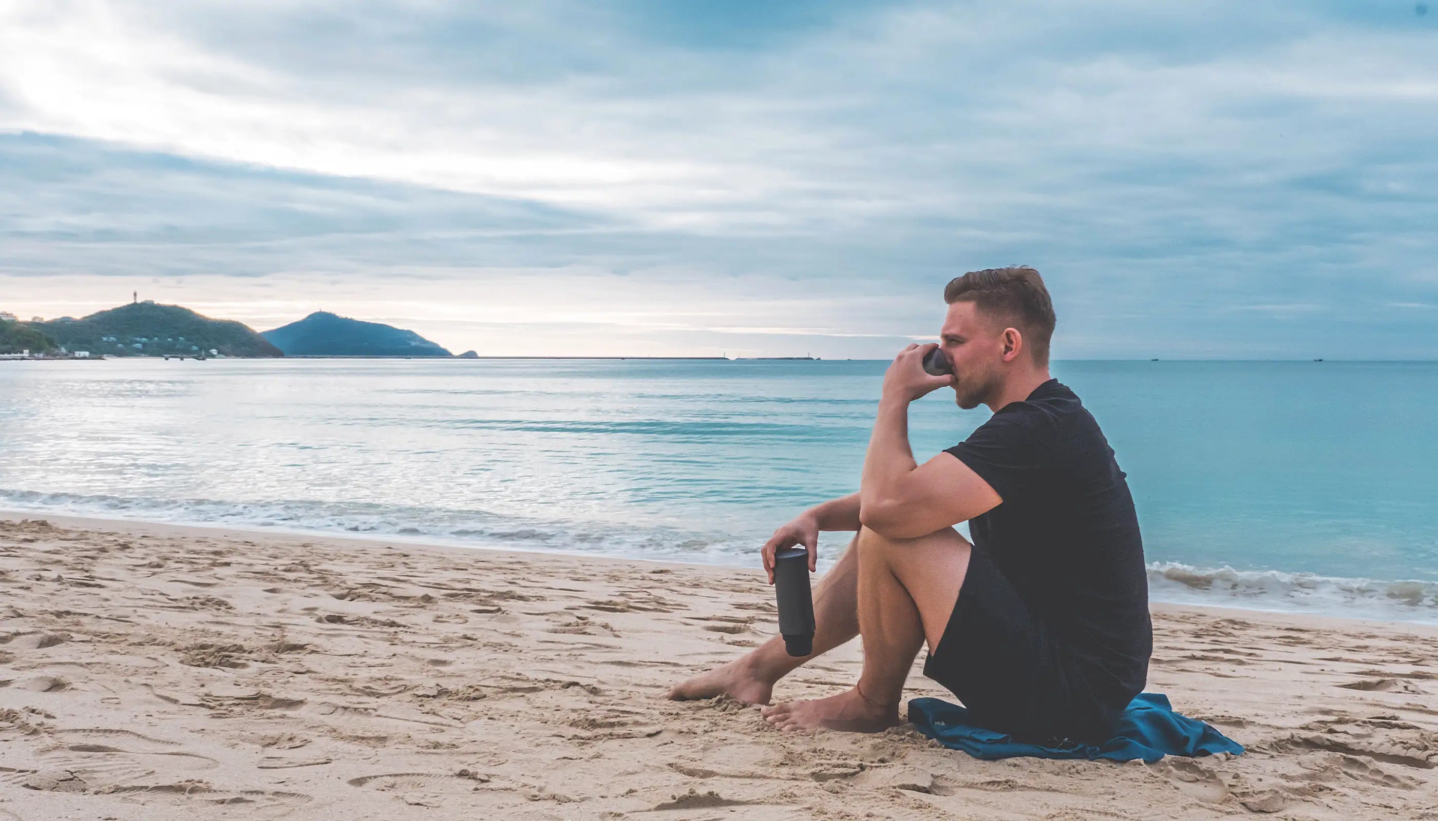 Mann entspannt am Strand mit Outin-Kaffeebereiter, genießt den Meerblick bei Sonnenaufgang, Outdoor-Kaffeegenuss am Meer