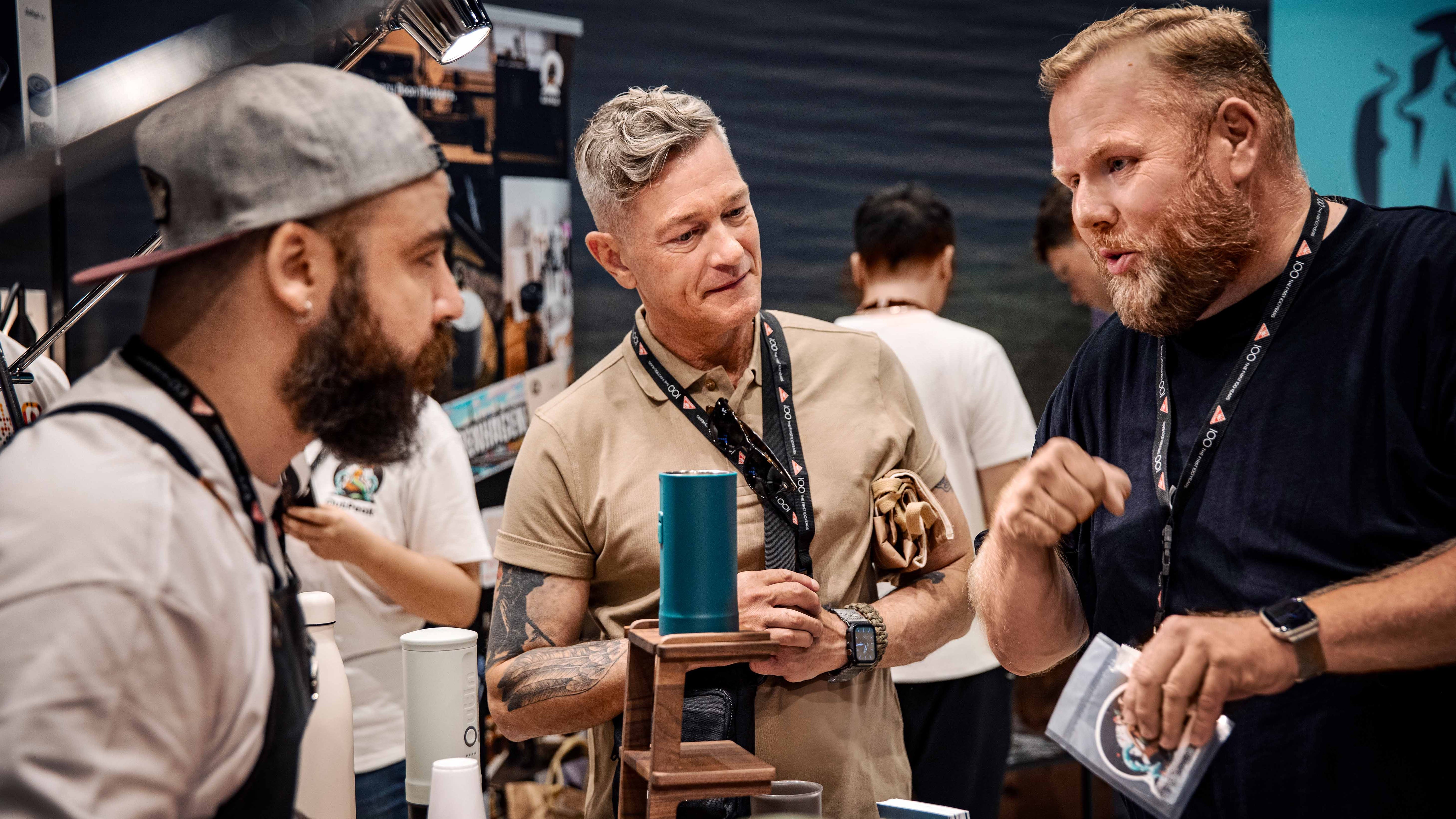 Gespräch unter Kaffeefachleuten am Messestand: Vorführung eines Brühgeräts, Austausch zu Espresso‑Technik, Mühle und Zubehör.
