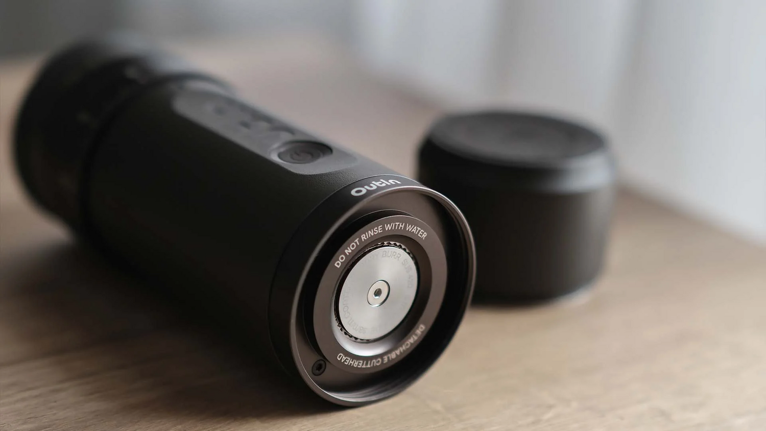 Nahaufnahme einer tragbaren elektrischen Kaffeemühle auf einem Holztisch mit sichtbarem Mahlwerk und minimalistischem Design