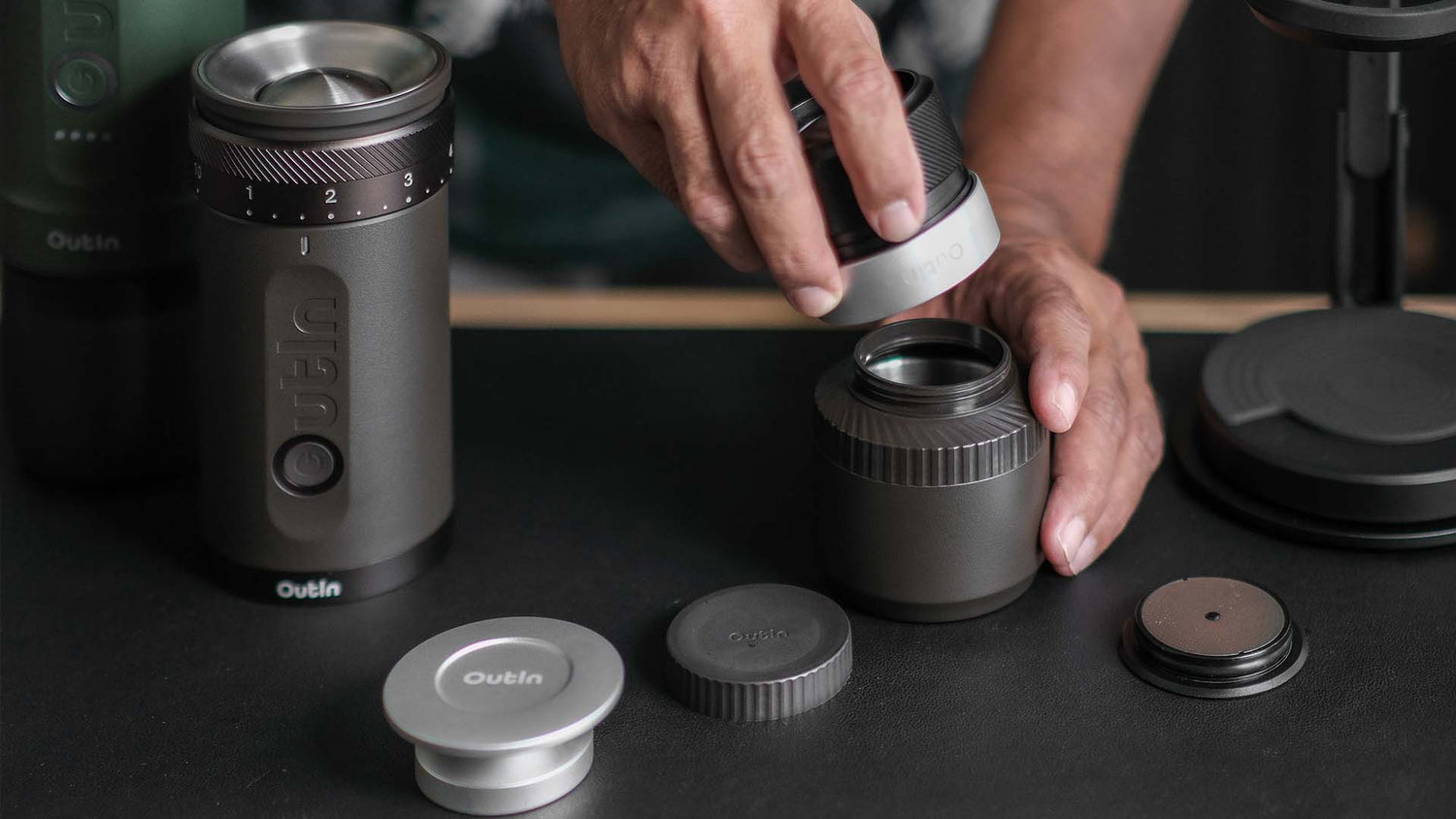 Eine Person baut eine dunkelgraue, tragbare Kaffeemühle der Marke Outin zusammen.