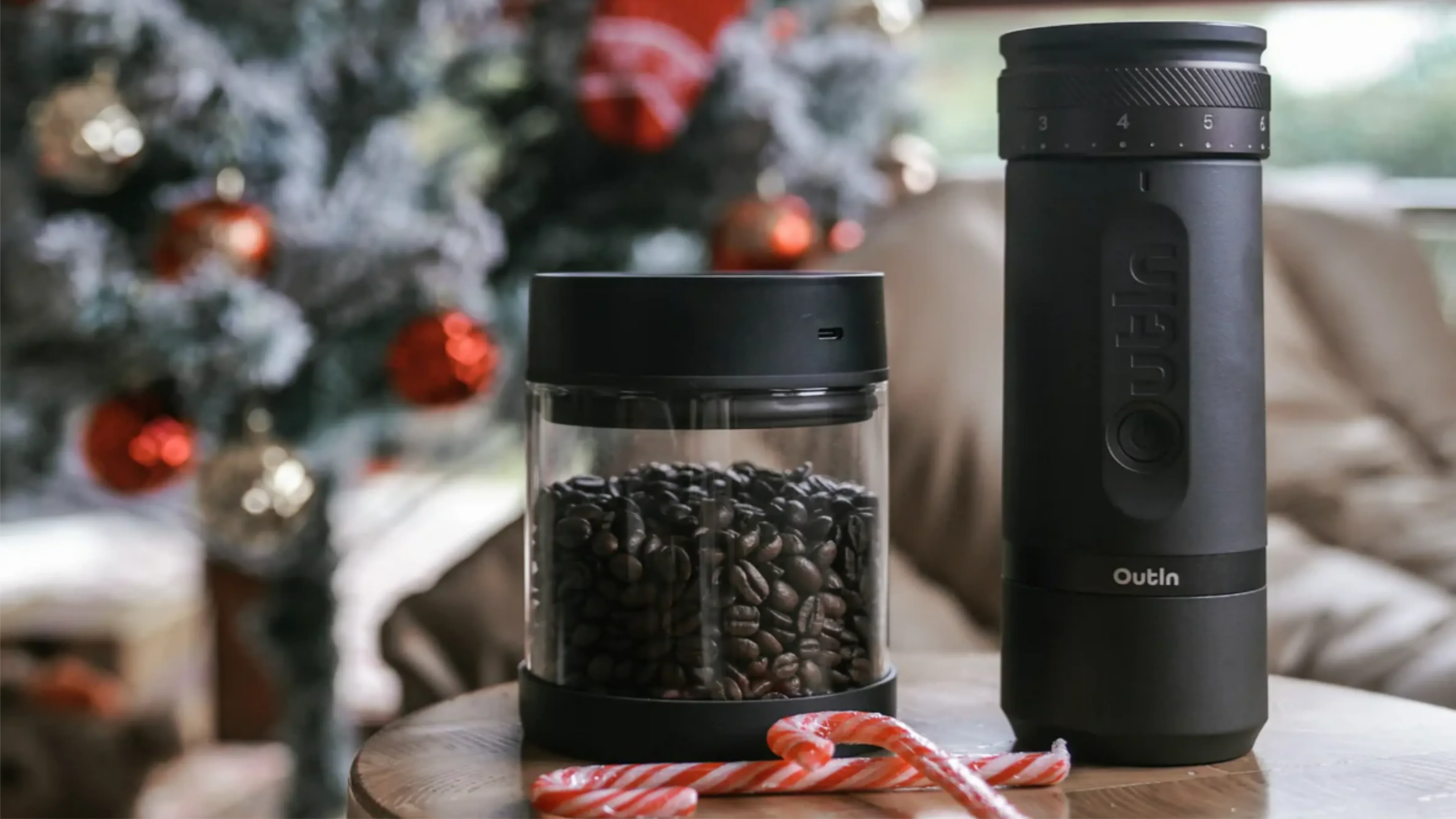 Outin elektrische Kaffeemühle und Vakuumbehälter mit frischen Kaffeebohnen, arrangiert vor festlicher Weihnachtsdekoration und Zuckerstangen