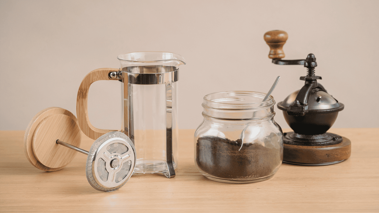 Komplettes Handbrüh-Setup mit French Press, nostalgischer Handkaffeemühle und Mason Jar voller Kaffeebohnen auf Holzoberfläche – rustikale Werkzeuge für die manuelle Kaffeezubereitung.