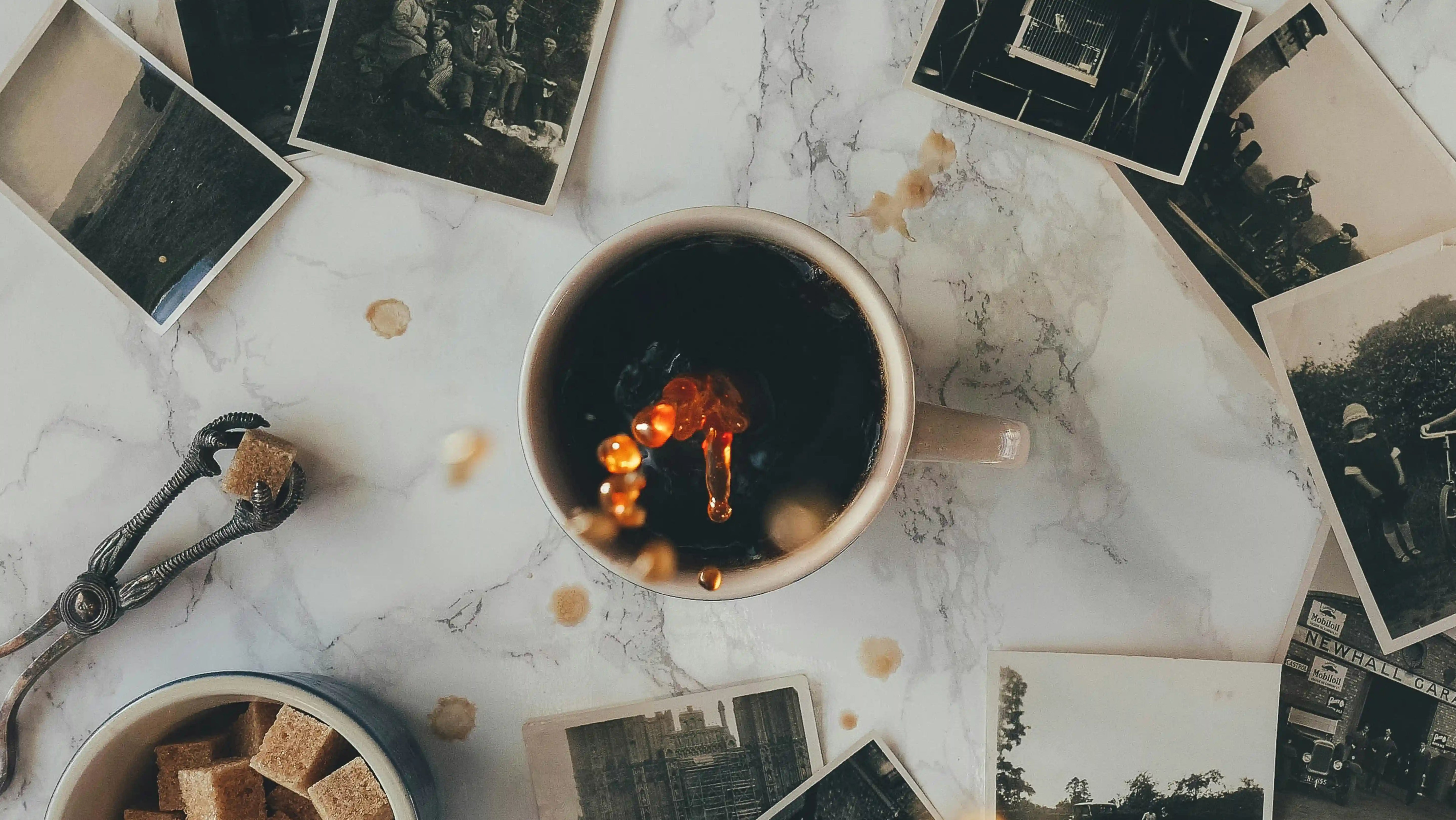 Cup of black coffee with vintage photographs scattered on marble surface, coffee droplets creating artistic reflections, nostalgic coffee moment