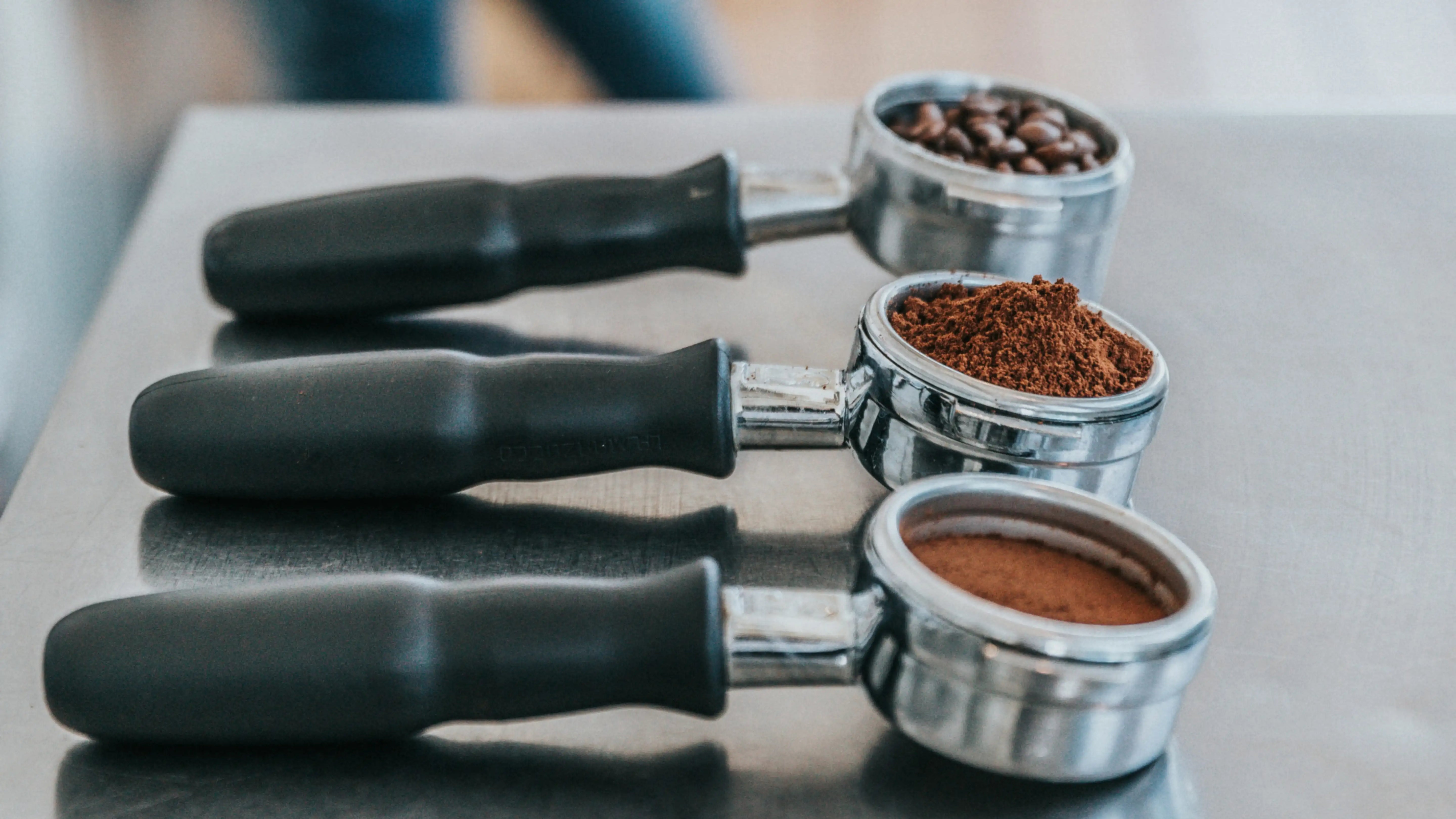 Drei Siebträger, gefüllt mit Kaffeebohnen, gemahlenem Kaffee und feinem Espressomehl.