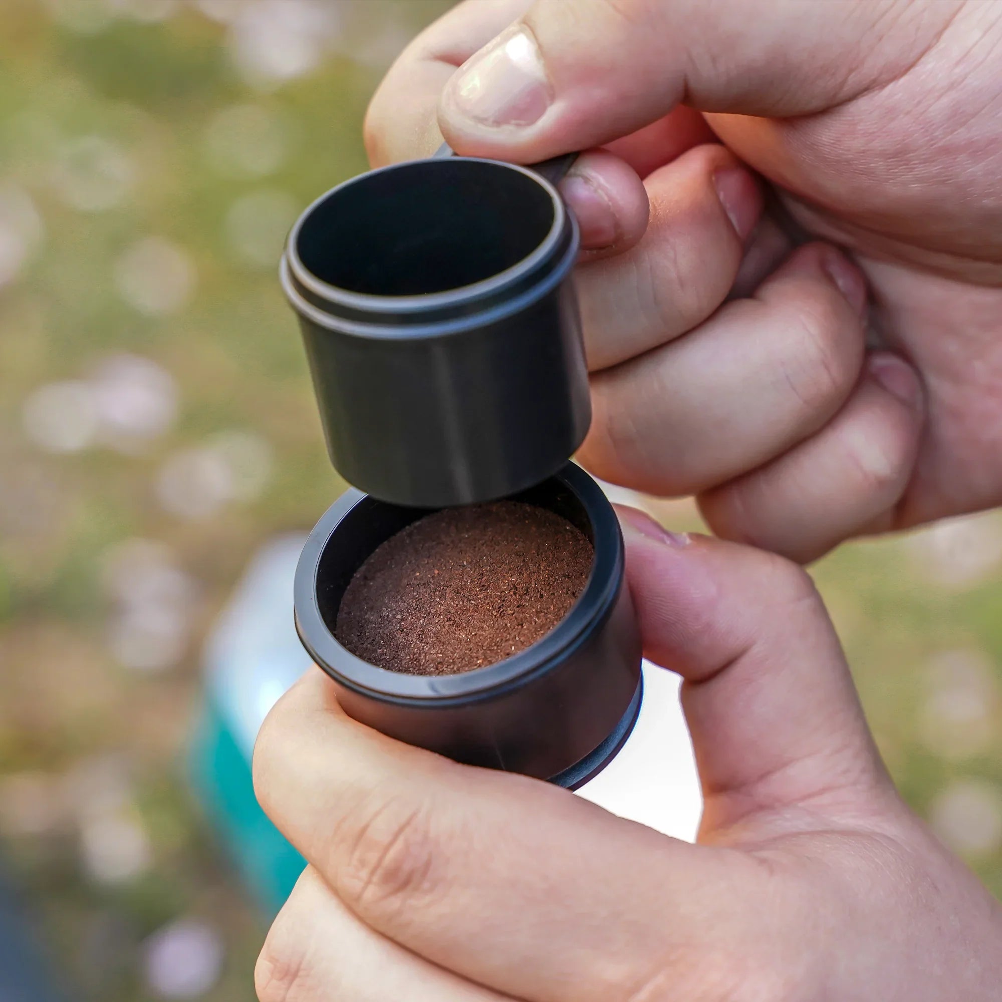 User holding black Ground Coffee Spoon over ground coffee filter for Outin Nano portable espresso machine