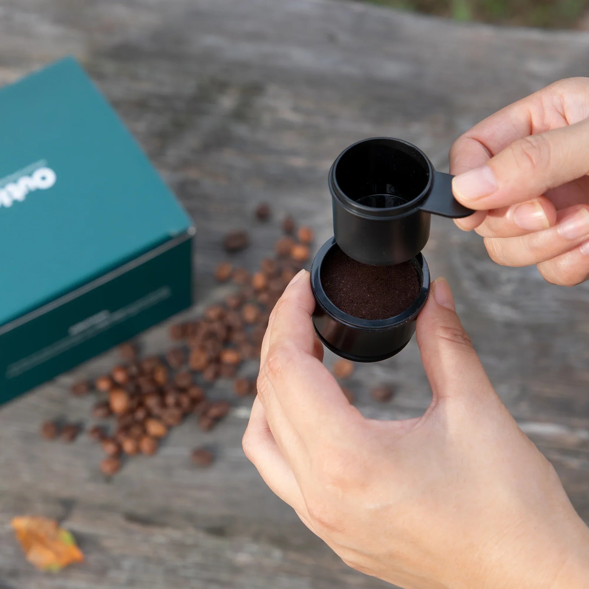 Filter Basket and spoon over ground coffee, with a teal box beside.