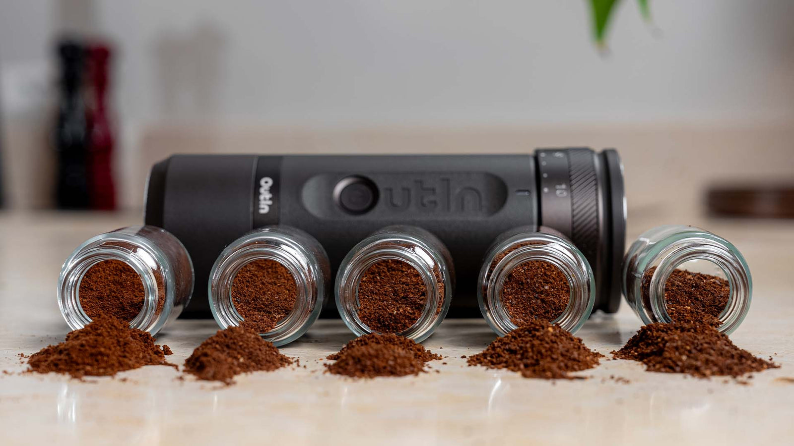Outin coffee storage system with five glass containers holding ground espresso on wooden surface.