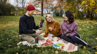 Eine Gruppe beim Picknick im Park, schwarze tragbare Kaffeemaschinen in der Hand, während sie den Herbst im Freien genießen