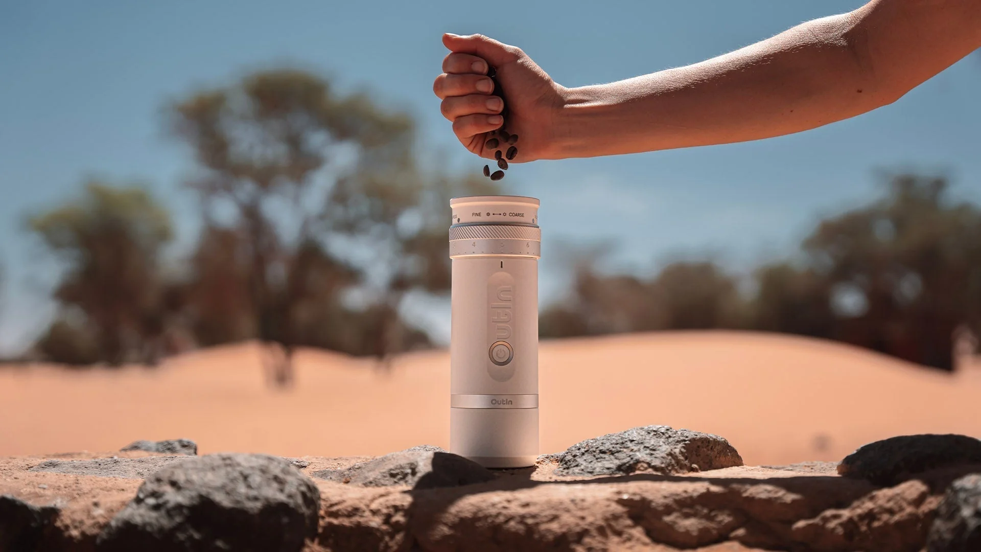 Kaffeebohnen in die tragbare Outin-Kaffeemühle geben für frischen Espresso bei einem Outdoor-Abenteuer in der Wüste.