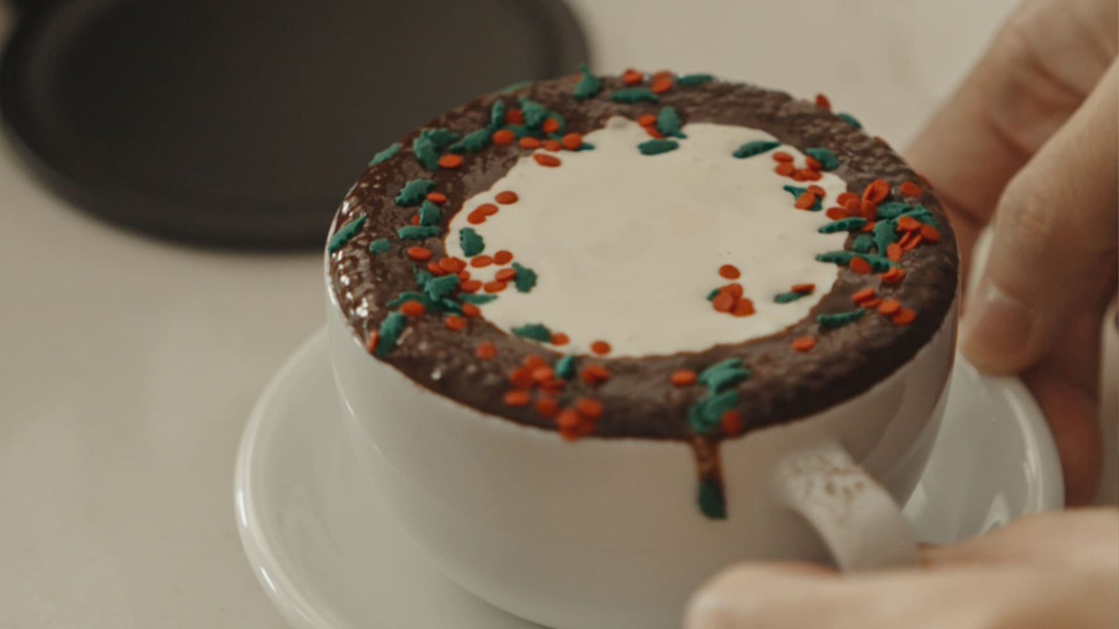 Weiße Kaffeetasse mit Schokoladentopping und farbigen roten und grünen Streuseln, kunstvoll arrangiert – ideal für festliche Kaffeevariationen jenseits der klassischen Milchversion