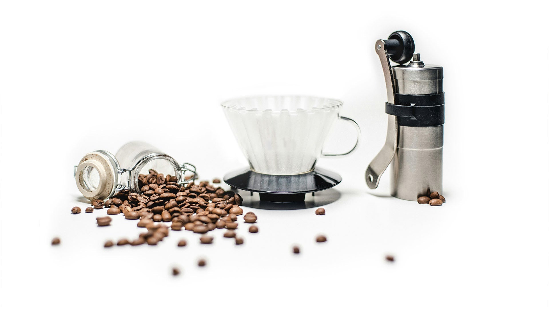 Komplettes Pour-Over-Kaffeeset mit Handkaffeemühle, Glasfilter und frischen Kaffeebohnen auf weißem Hintergrund – minimalistisches Arrangement von Kaffeezubehör.