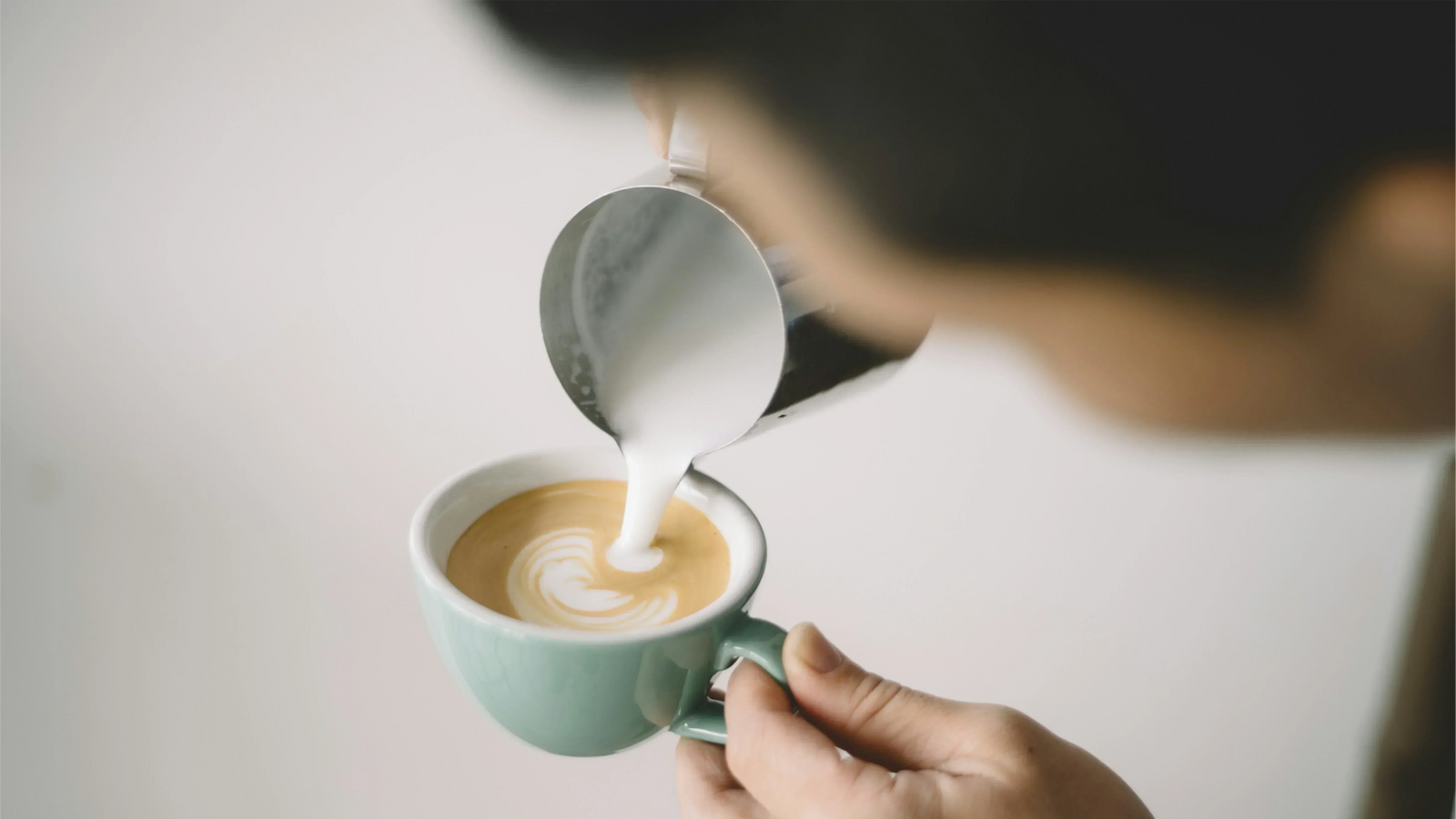 Aufgeschäumte, fettarme Milch wird in eine mintgrüne Tasse gegossen, um Latte Art zu kreieren. Dies demonstriert die richtige Technik zur Zubereitung eines Skinny Latte mit der Textur von cremigem Mikroschaum