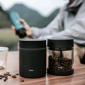 Outin Portable Electric Vacuum Coffee Canister, with coffee beans and a person holding a tumbler