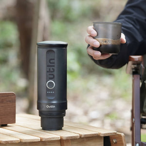 Outin Nano Portable Espresso Machine in black with freshly brewed espresso held outdoors