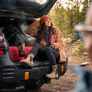 Woman enjoying coffee outdoors with fuchsia Nano Portable Espresso Machine at a car tailgate.